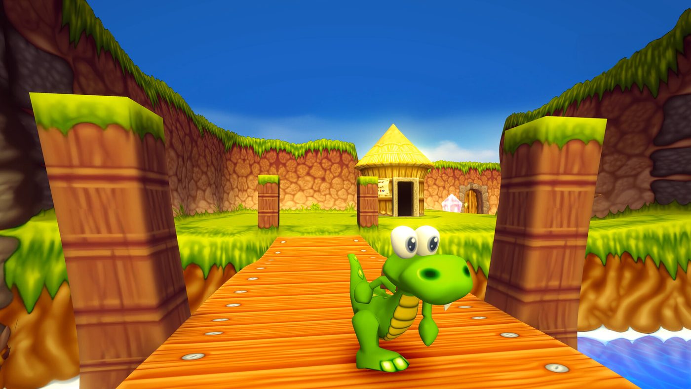 Croc stands on a wooden walkway above blue water, with grass banks and a thatched hut behind him